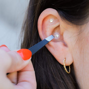 Goldene Ear Seeds, verziert mit Swarovski® Steinen, werden mit Hilfe einer Pinzette am Ohr angebracht.